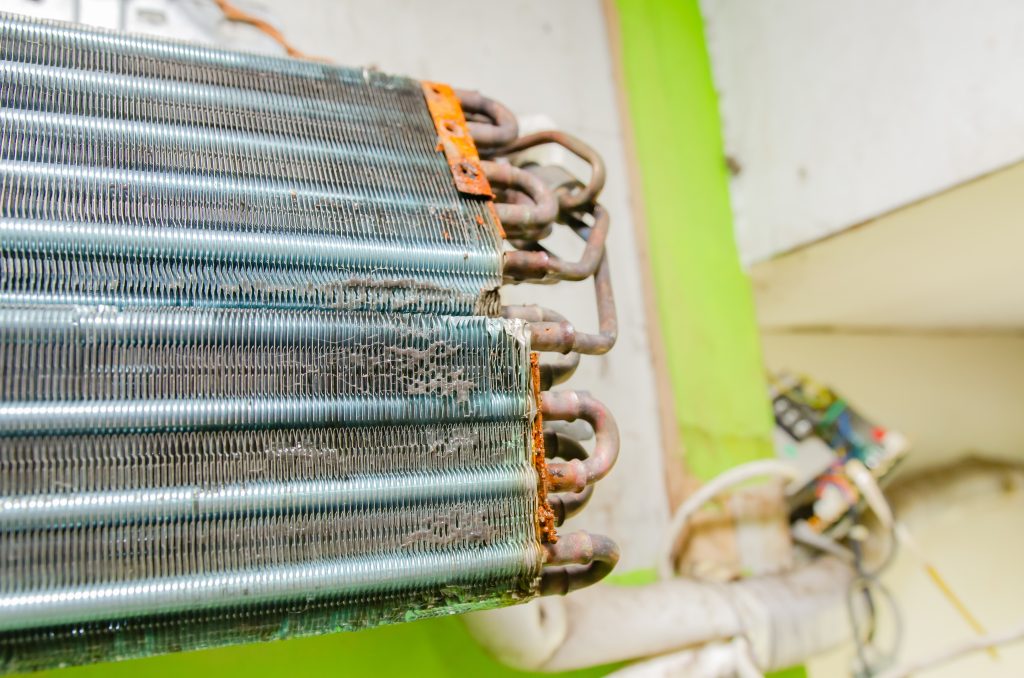 A close-up view of a severely rusted and corroded metal air conditioner coil, illustrating the type of hidden damage that can impact AC repair cost in the Florida Panhandle.