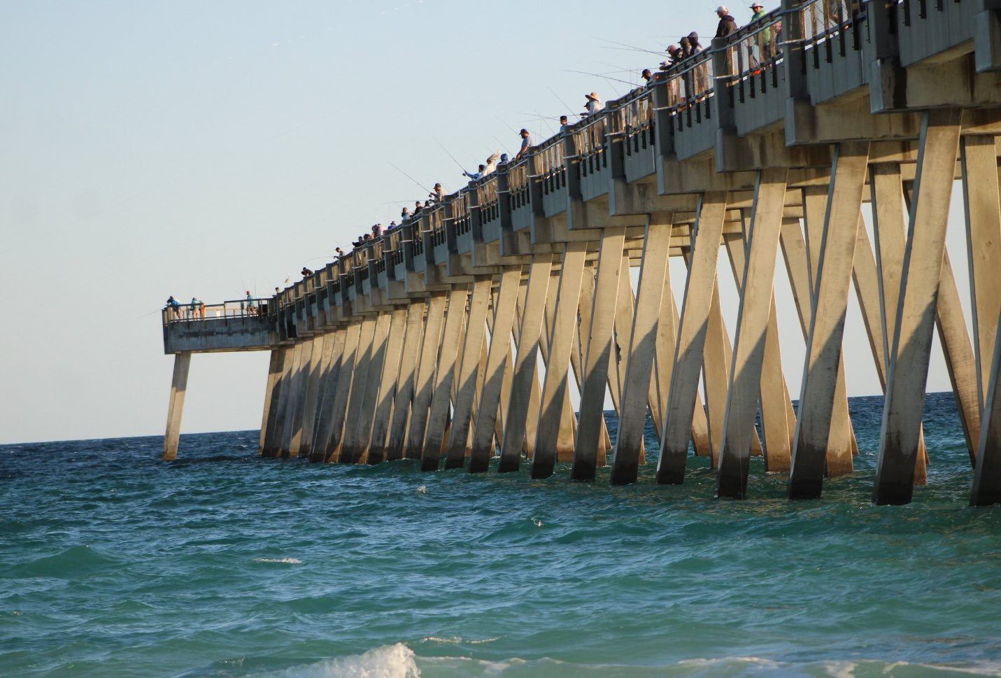 a florida peir in mid day with dozens of people standing on it looking out at the water