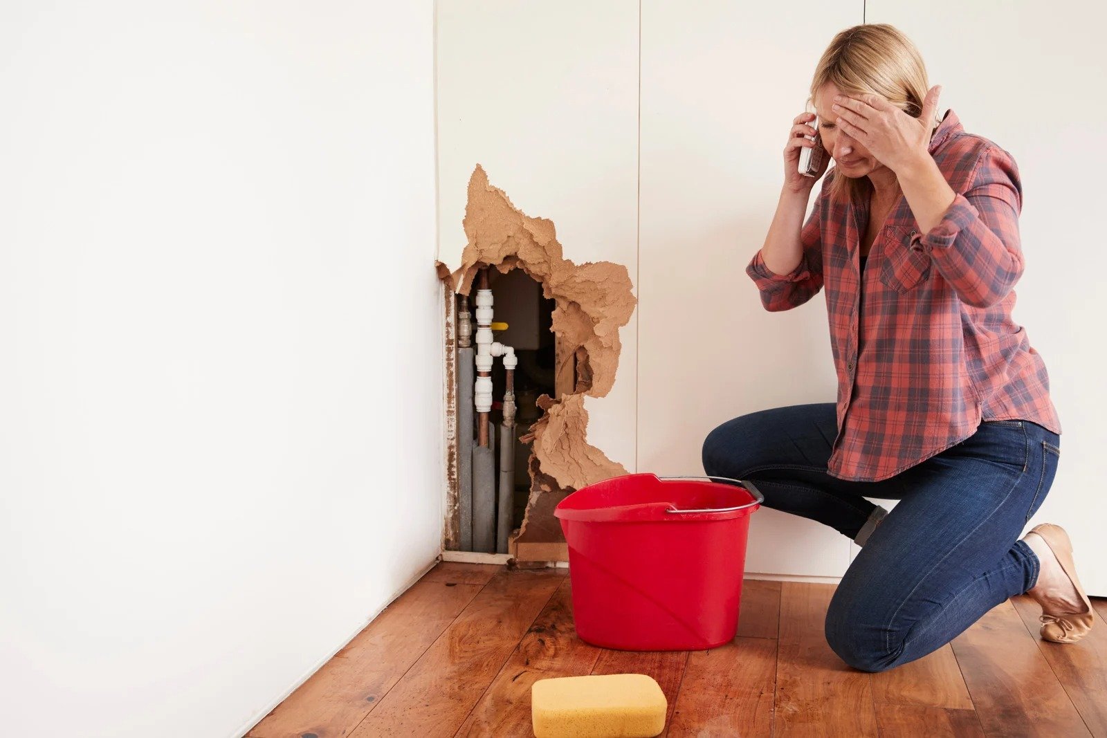 a home owner distraught by a water leak trying to clean up using a sponge and red bucket