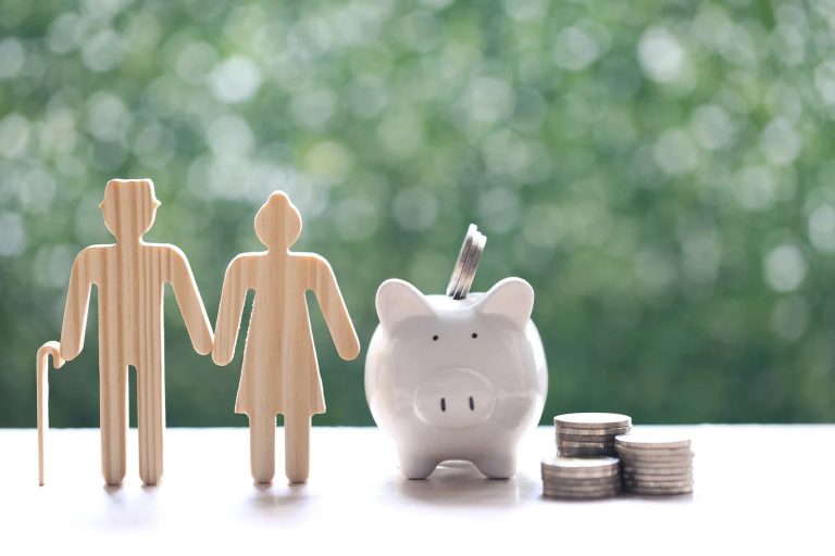Wooden cut-outs of a family standing next to a white piggy bank and small stacks of coins.