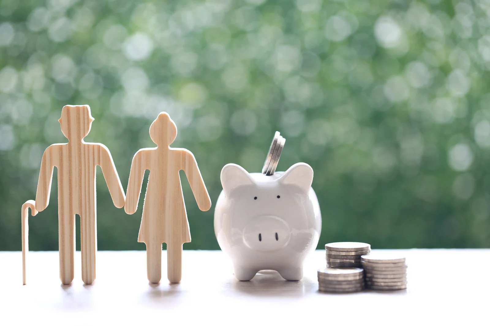 Wooden cut-outs of a family standing next to a white piggy bank and small stacks of coins.