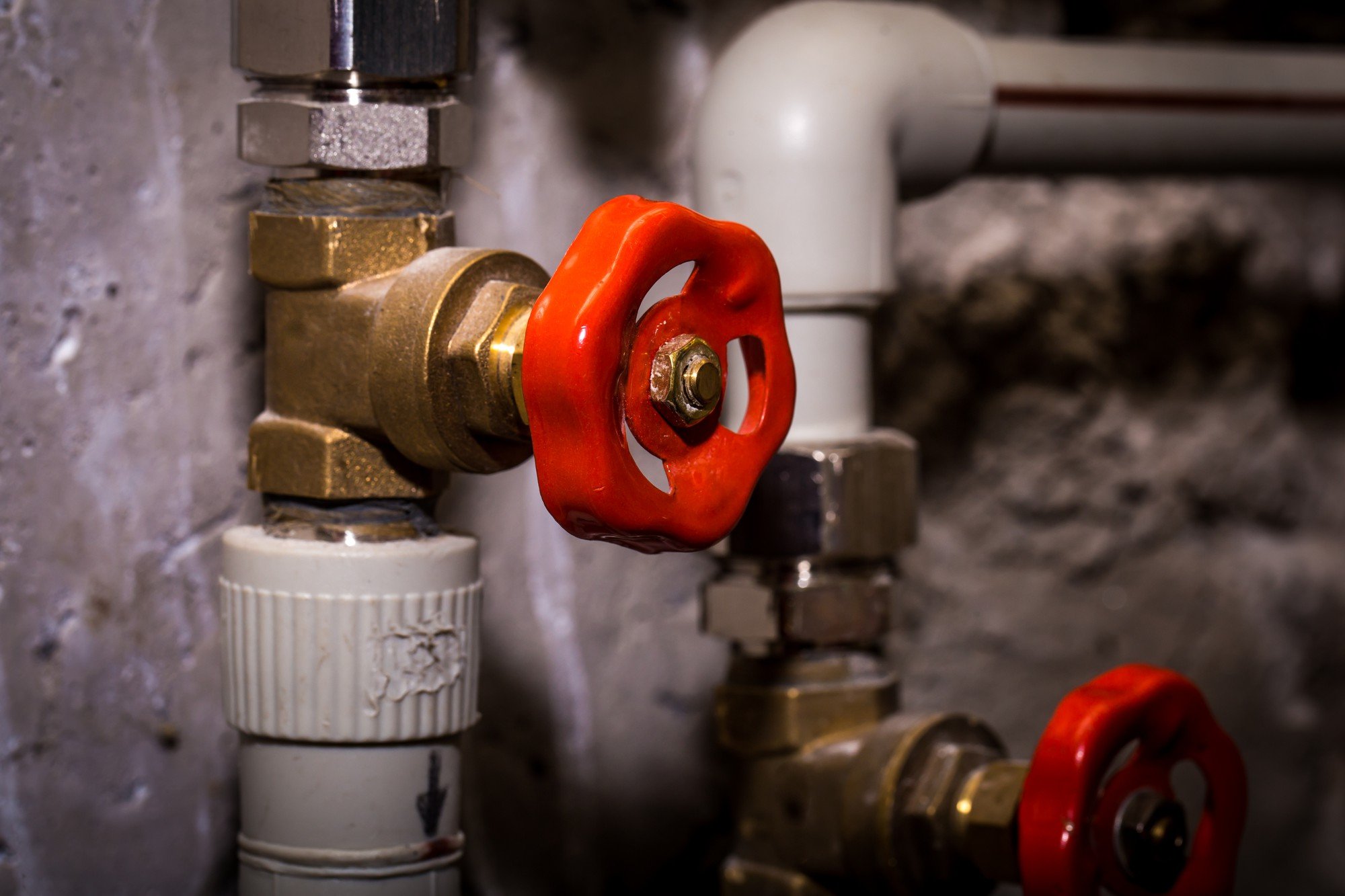 A close-up shot of a heavy-duty brass water shut-off gate valve with a red circular handle installed on a white PVC pipe.